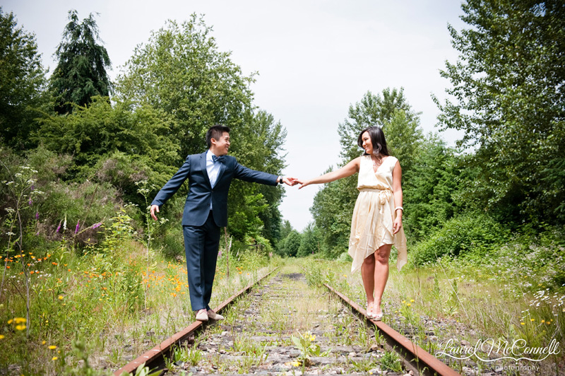 Couple holding hands on train track near forested area of Seattle area winery.